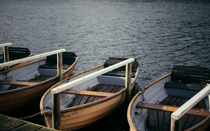 three row boats are sitting on the dock by the water