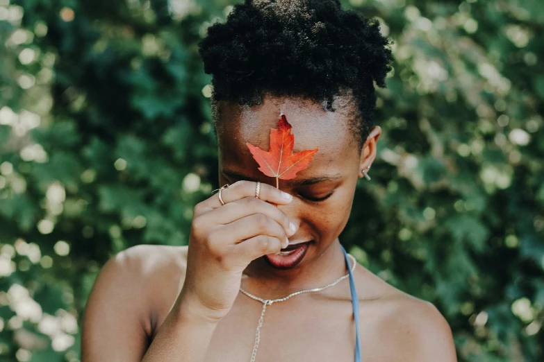 a young woman holding a single orange leaf on her nose