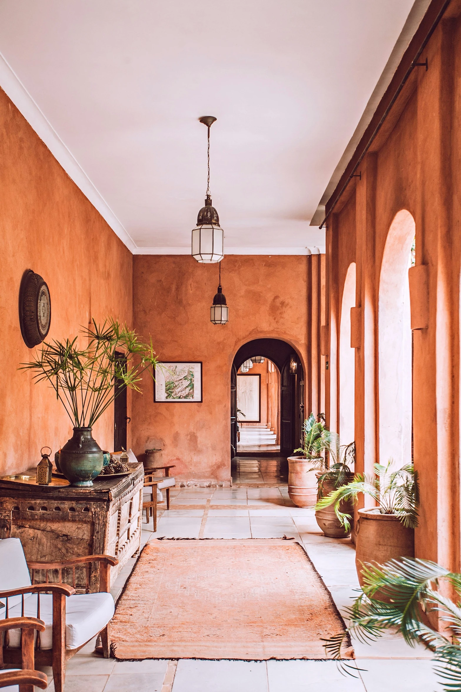 there is a large room that has an arch to the left and plants on the floor in pots to the right