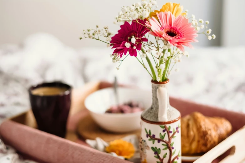 a tray on a bed filled with bread and a vase with colorful flowers