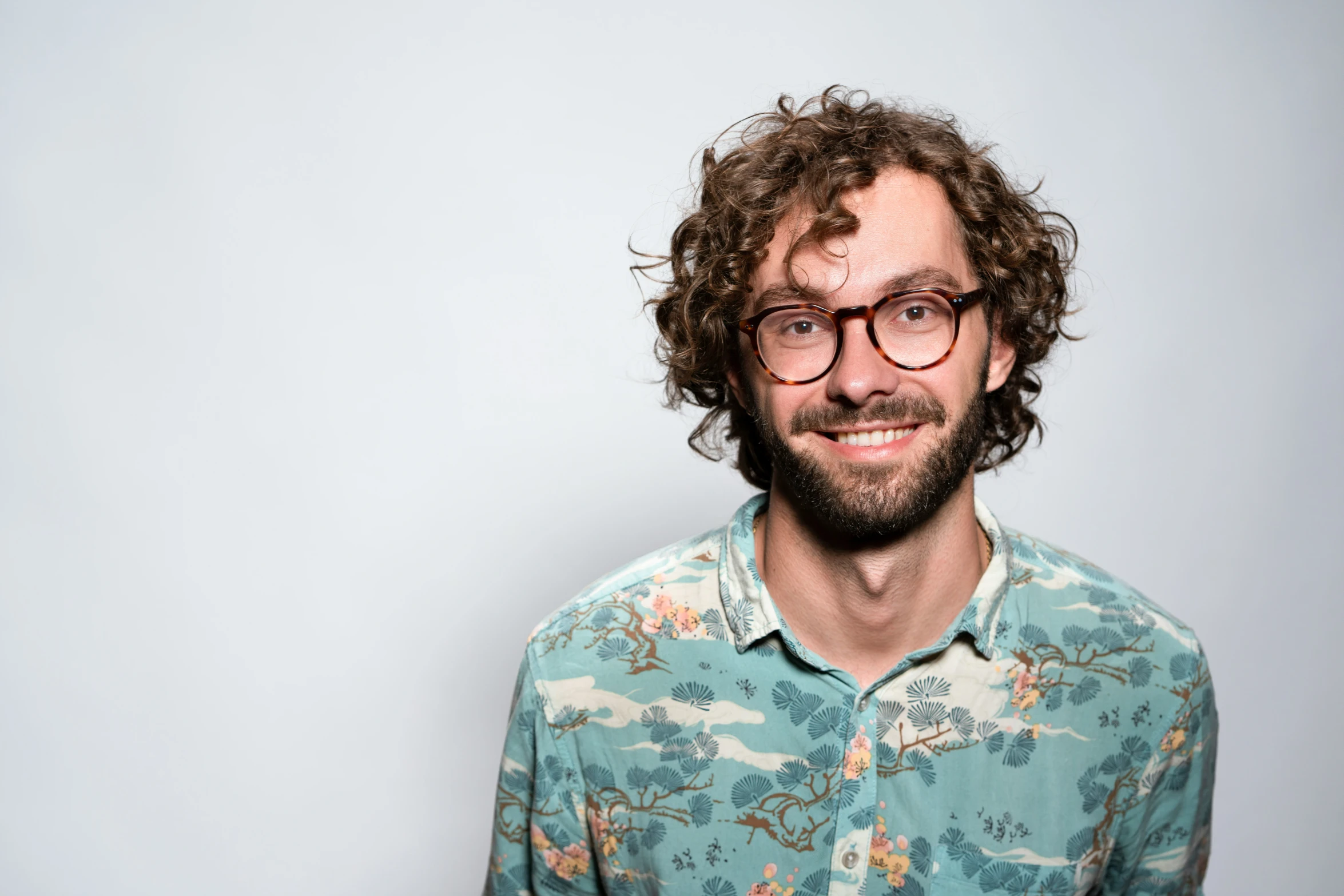 a man with curly hair and glasses smiles into the camera