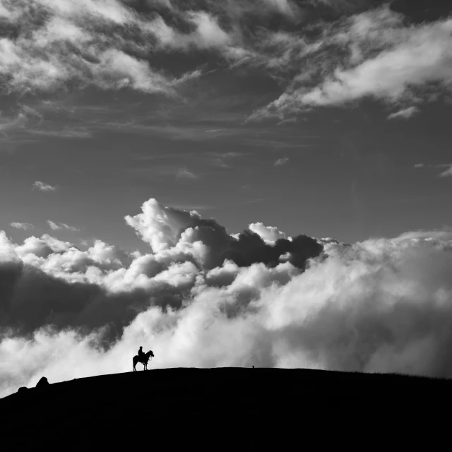 a person on a horse riding on top of a hill with clouds