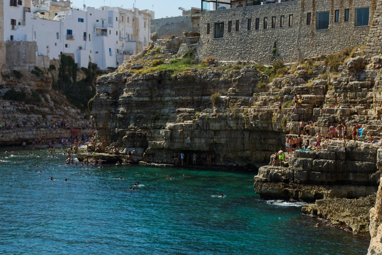 a group of people swimming in the ocean next to a rocky cliff