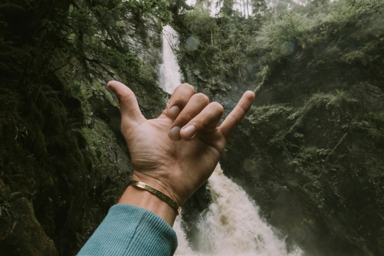 a man's hand with his outstretched out in front of a waterfall