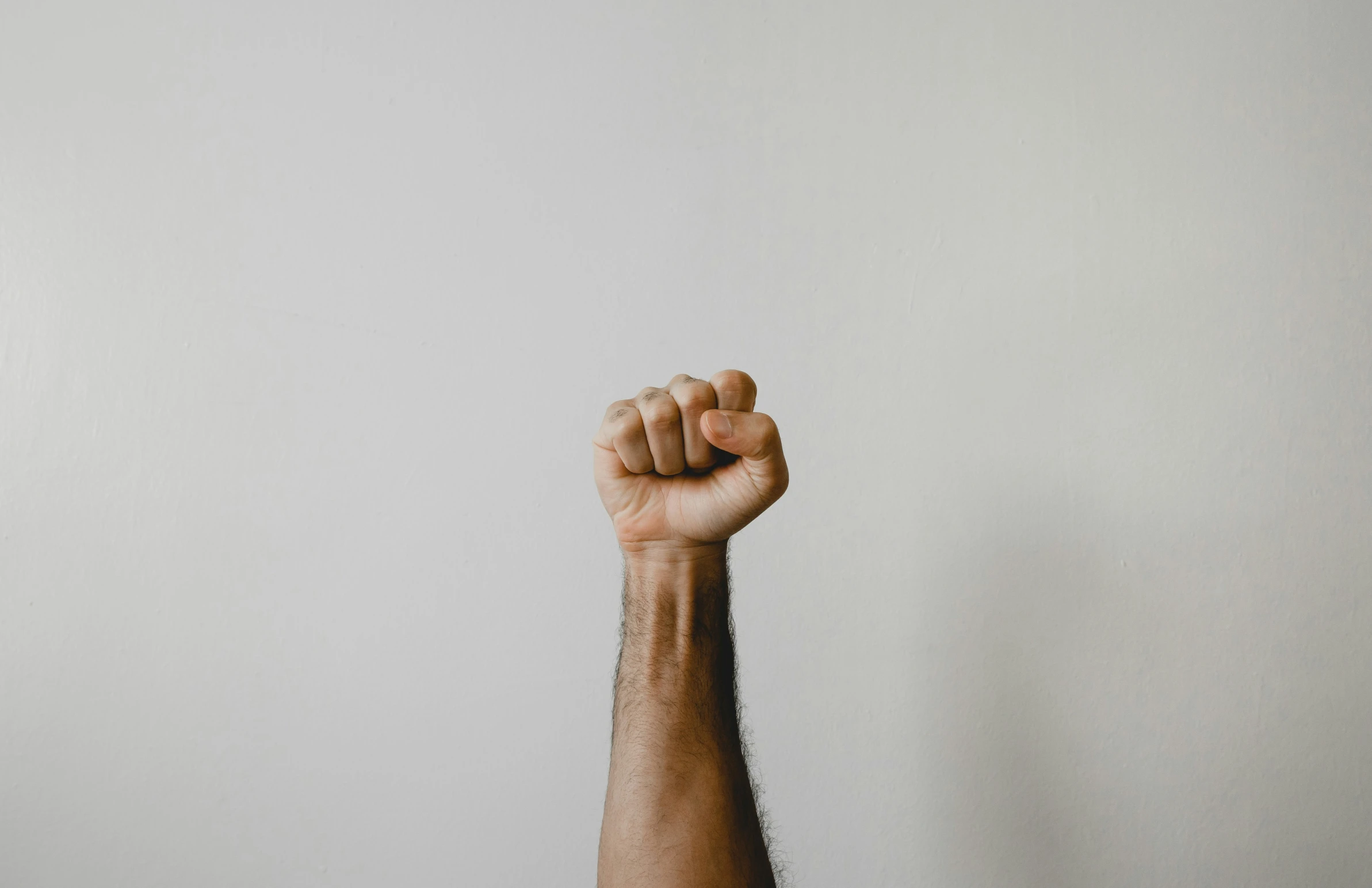 an arm with a fist raised in front of a white wall