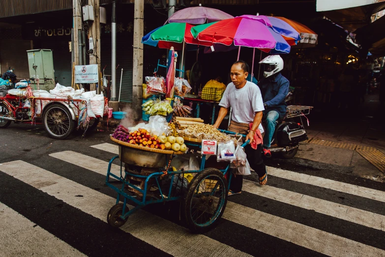 people standing in the street looking at some fruit on a cart