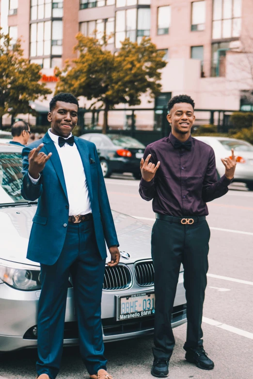 two men stand near the front of a parked car