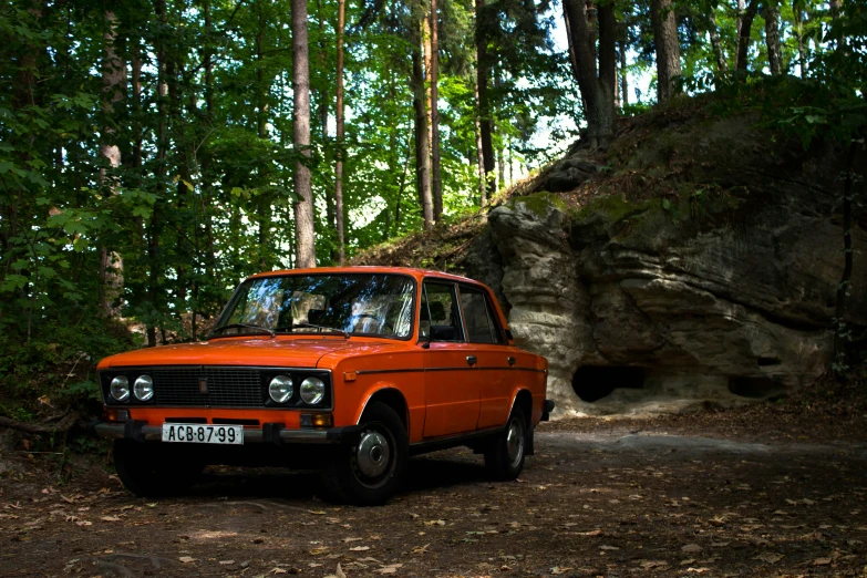 an orange vintage car parked in front of rocks and trees