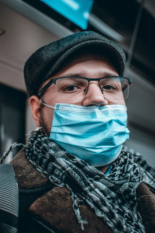 a man with glasses and a cap is wearing a blue face mask