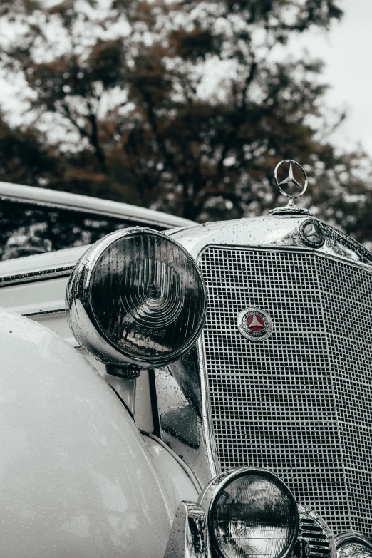 an old car with its headlights on is in front of a tree