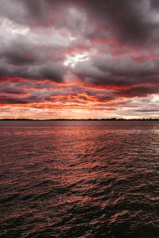 the sun is setting over water with dark clouds