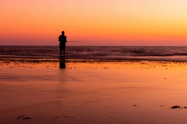 the silhouette of a person standing on the beach at sunset