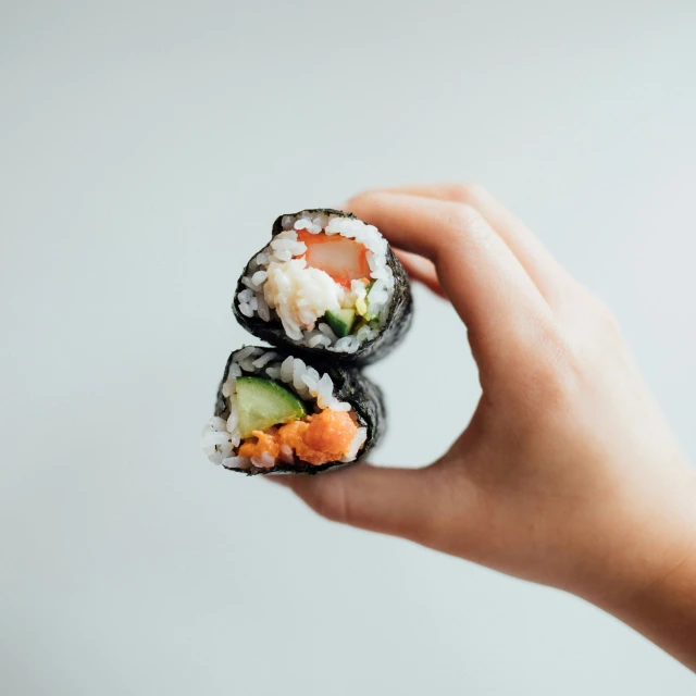 a hand is holding sushi, a small part is filled with salmon and cucumber