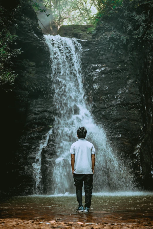 man standing at waterfall overlooking area with rock wall