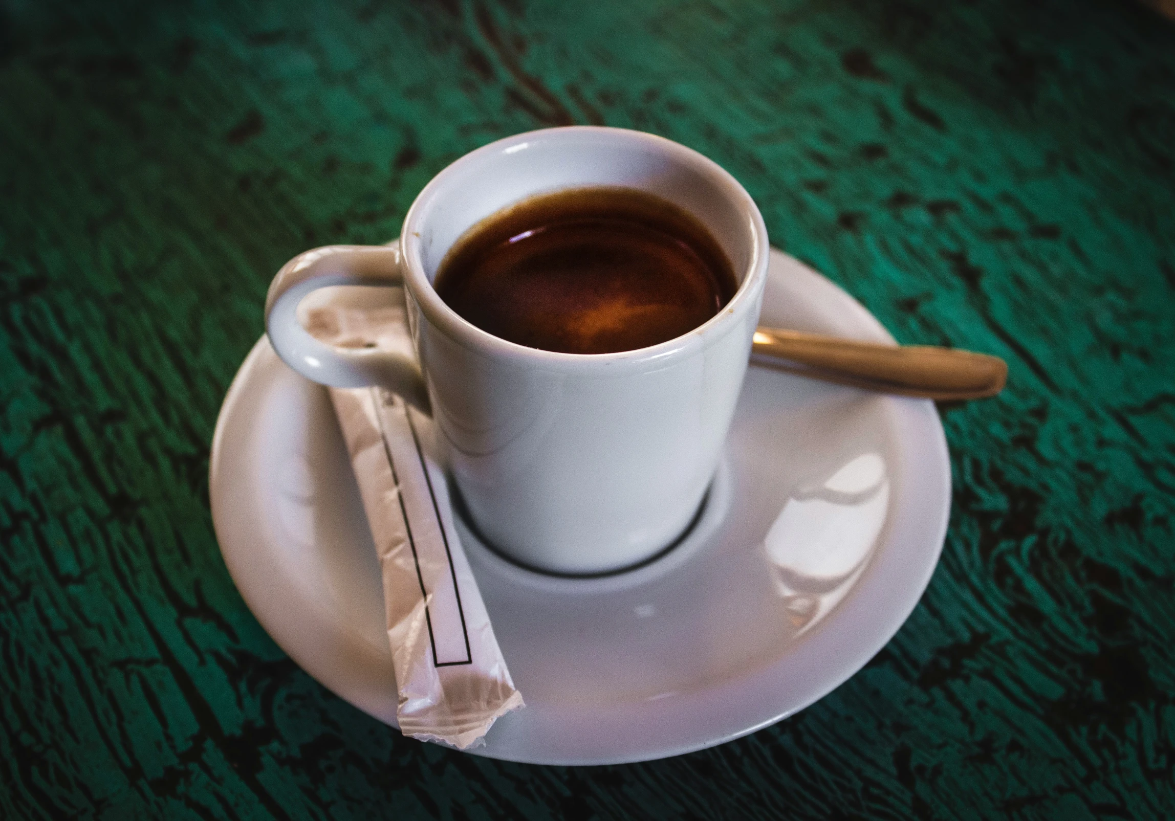 a cup with some coffee and a spoon on a green table