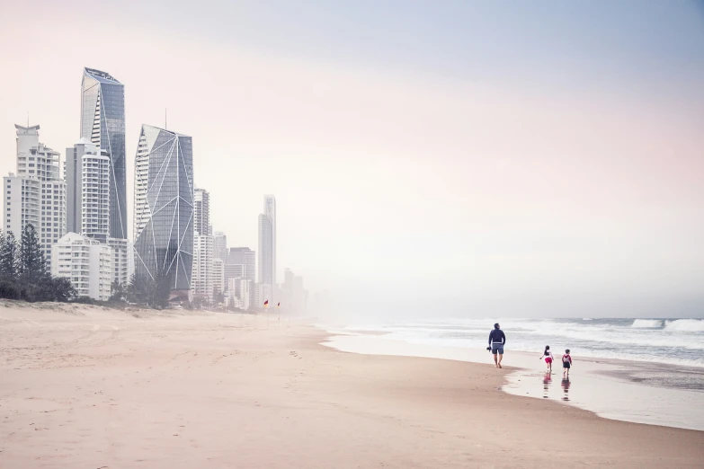 two people on the beach walking towards a city