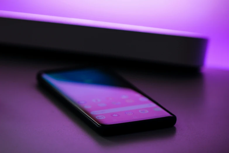 a purple and black smartphone sits on a dark table