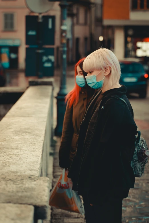 two people with protective masks standing on a sidewalk