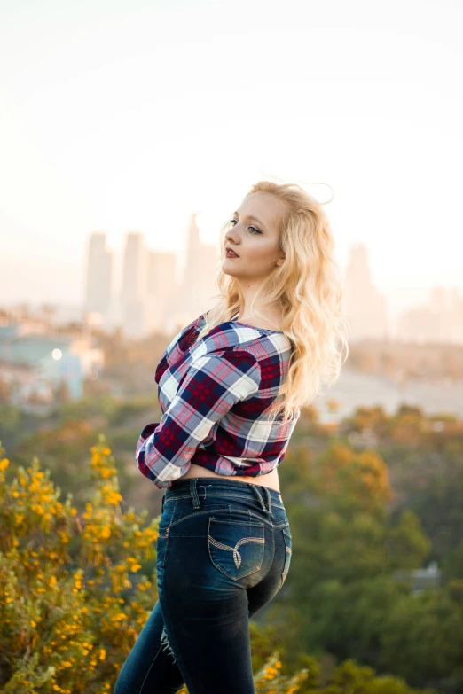 young lady standing on edge of cliff with city in background