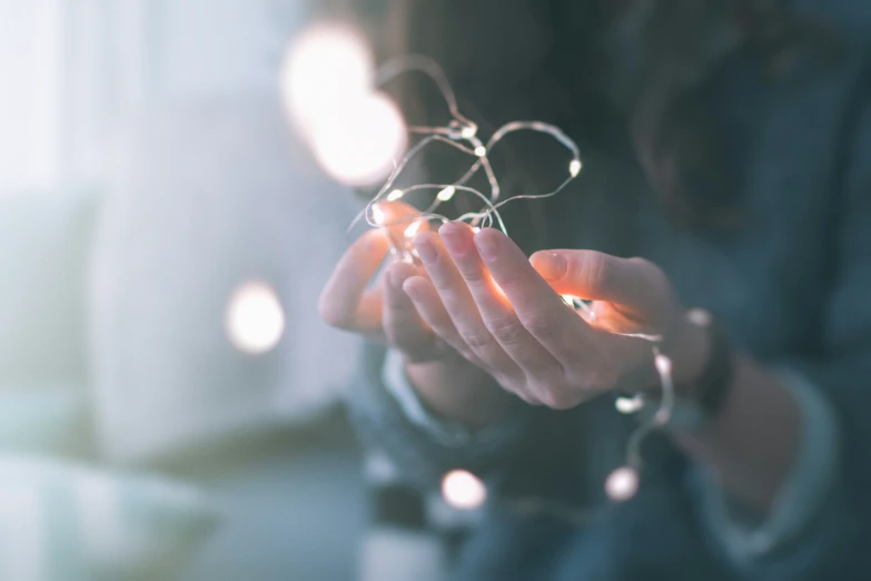 a woman holding her hand with some string lights hanging from it