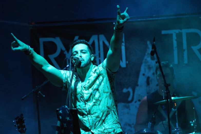 a man on stage singing with his hand raised and the fingers up