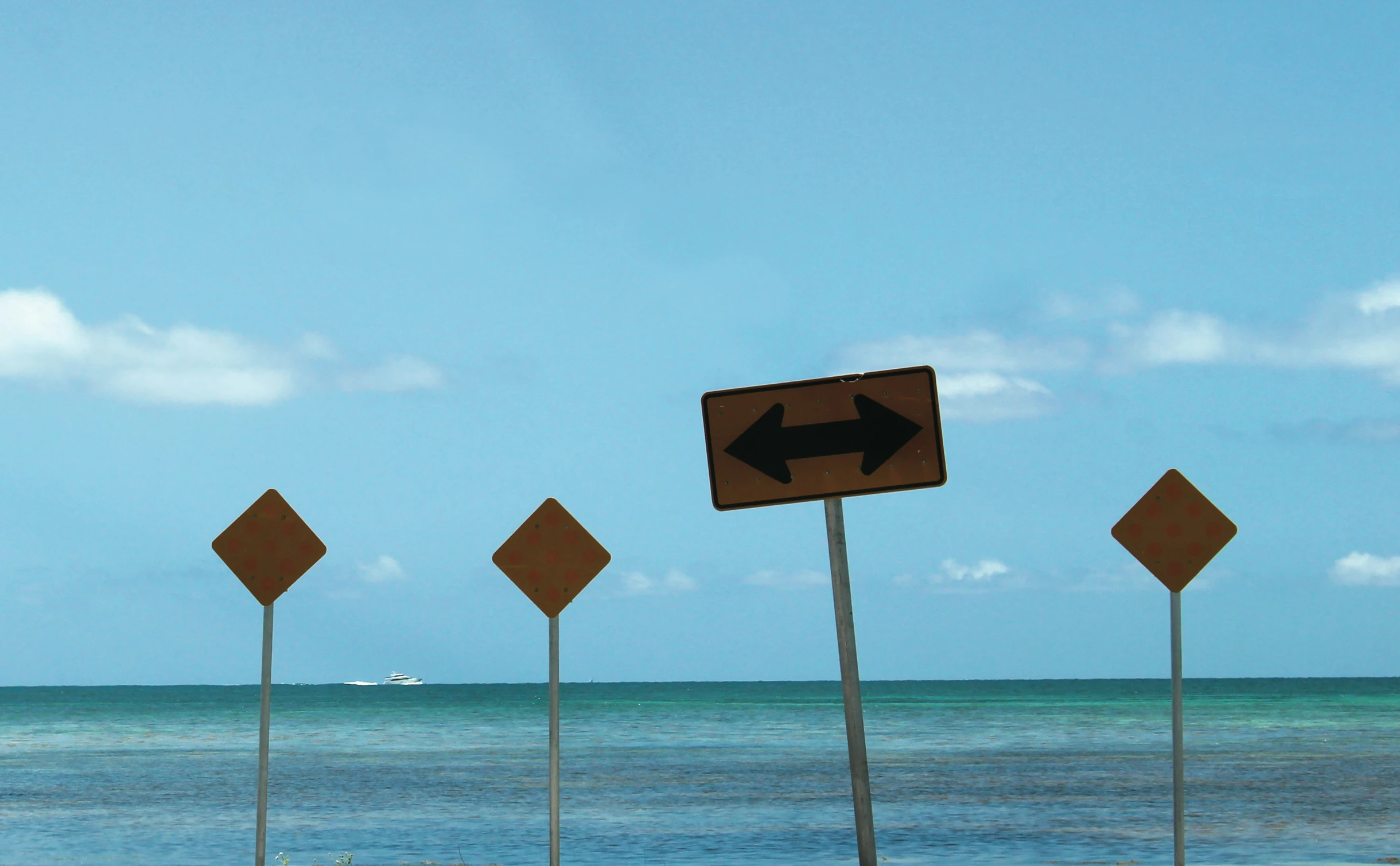 five road signs next to the beach with ocean and blue sky