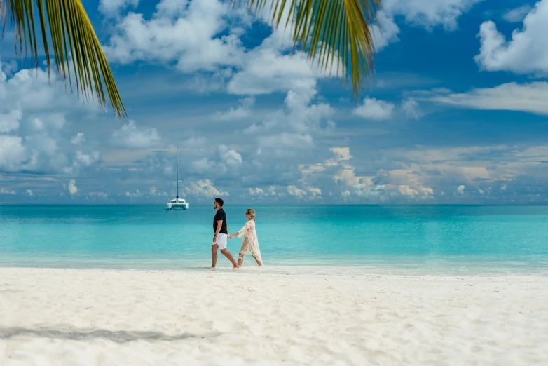 two people walking on the beach with the boat in the water
