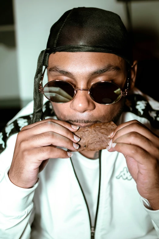 a young man eats a piece of food while wearing sunglasses