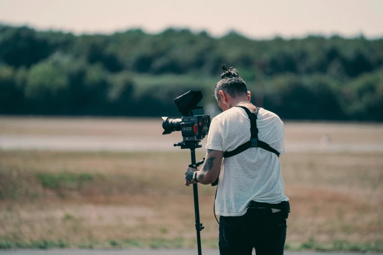 man in white t - shirt behind a camera on a tripod