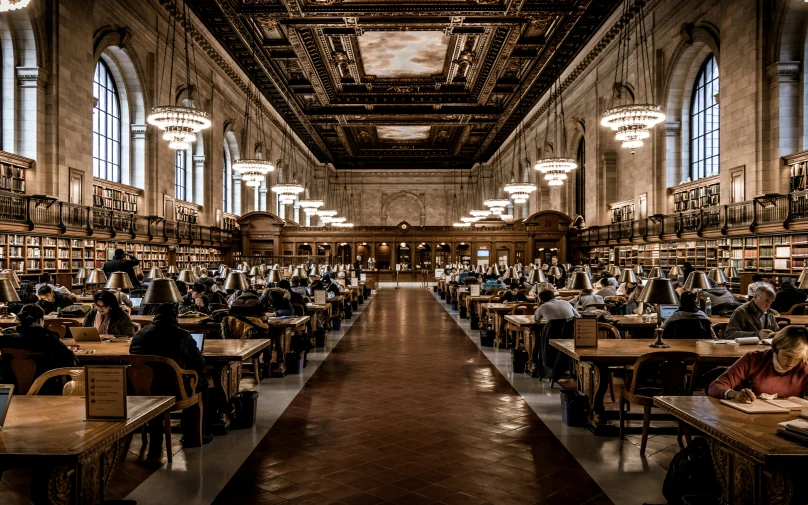 people in a public liry reading books on the desks