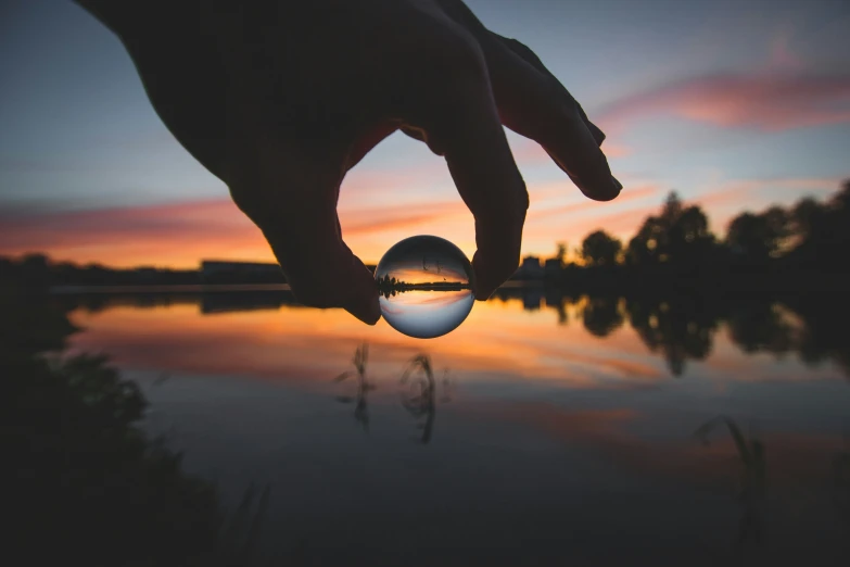 person holding ball above body of water at dusk