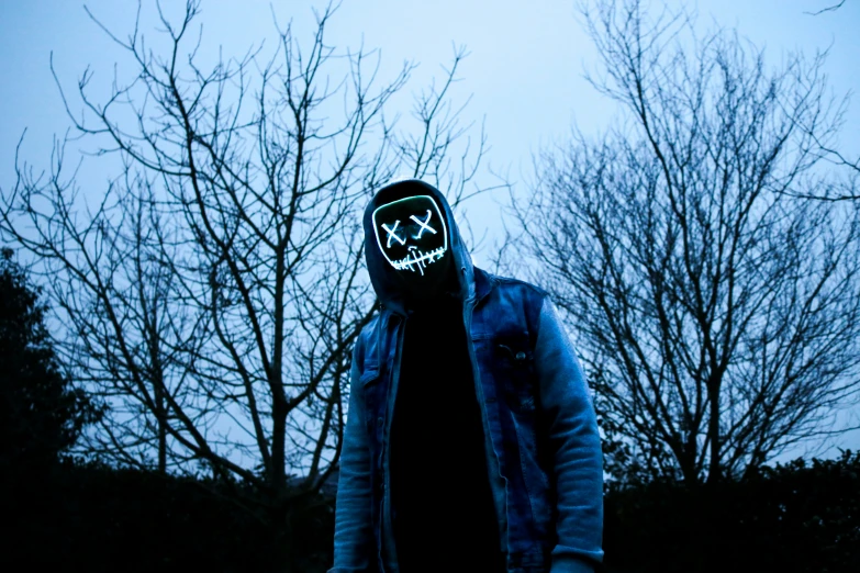 a person with a hoody covered with a mask stands with a skateboard