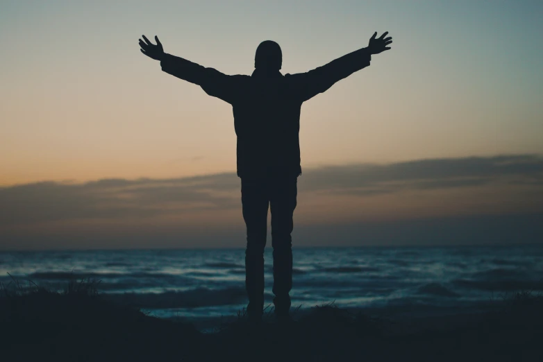 a man is standing in the sunset with his arms outstretched