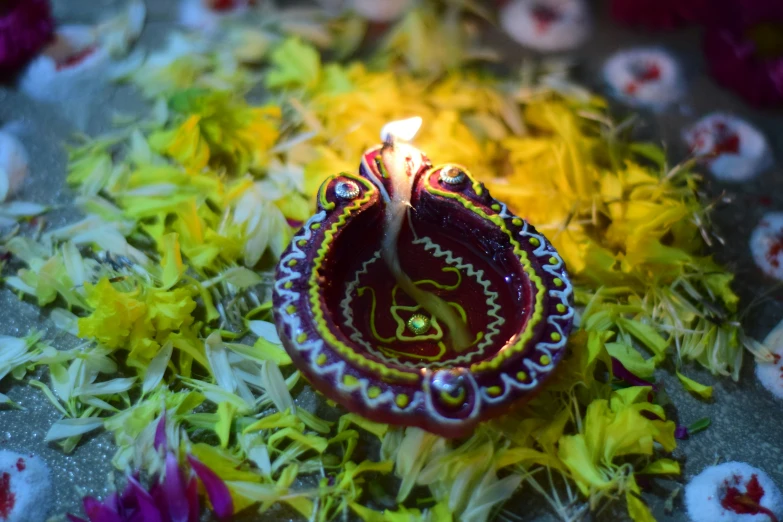 a lit oil lamp on the ground filled with flowers