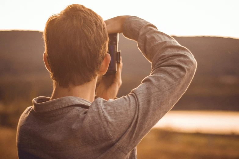 a young man holds his cell phone up to his head as he stands by a river