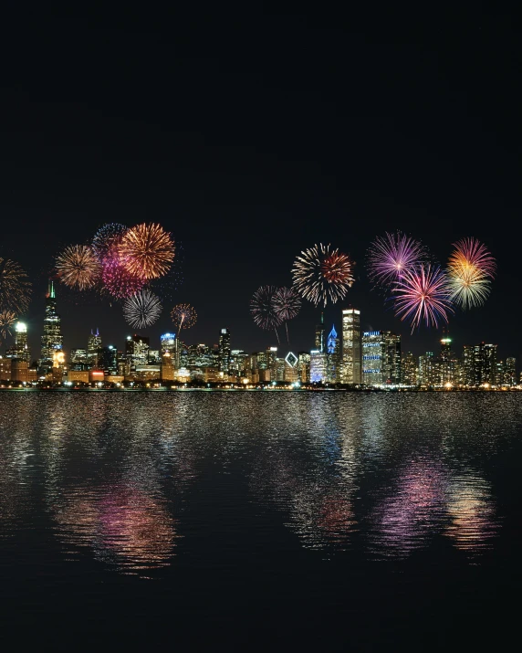 a city skyline at night with fireworks and reflection in the water