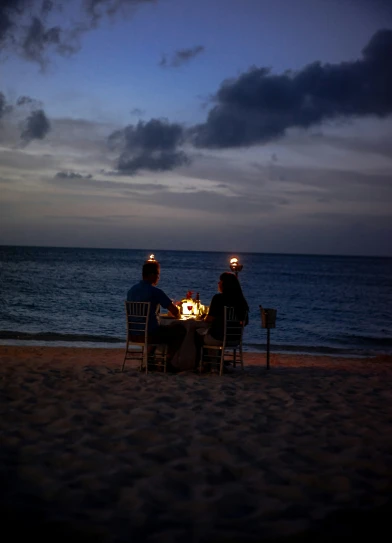 two men are eating while sitting on the beach
