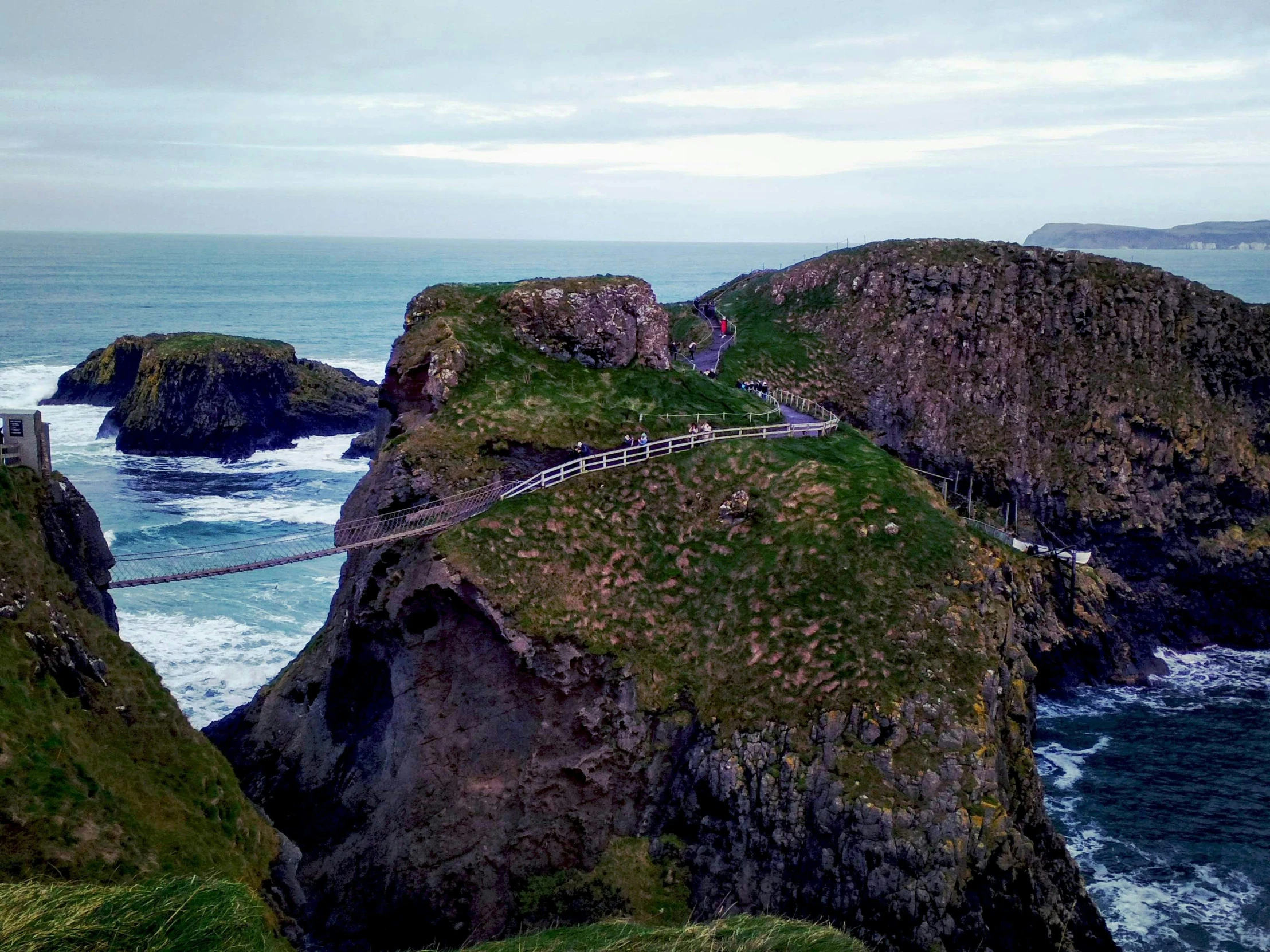 people walk on the walkway near a rocky cliff near the ocean