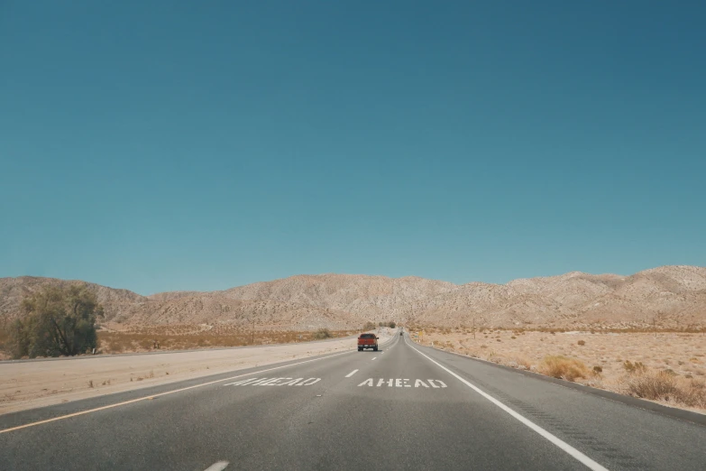a van driving down an empty road with desert hills in the background