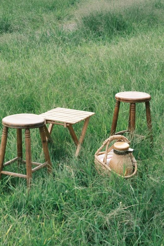 three wooden stools are in the grass next to an old basket