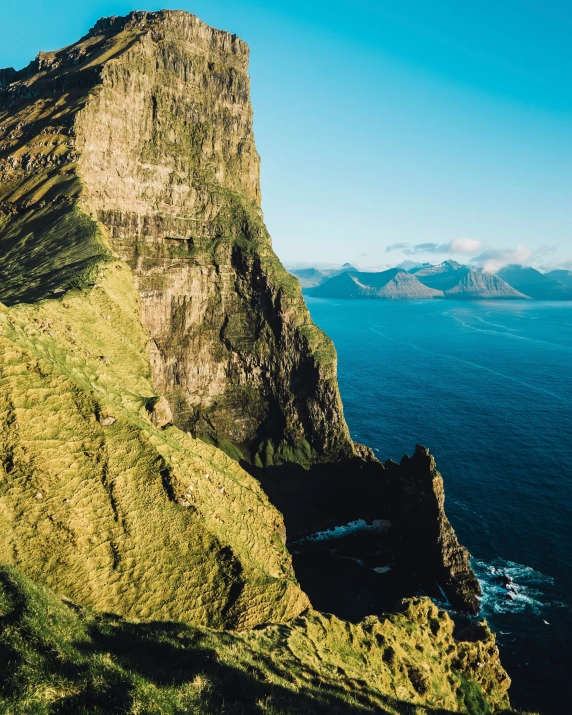 a large steep cliff with green grass and a body of water in front of it