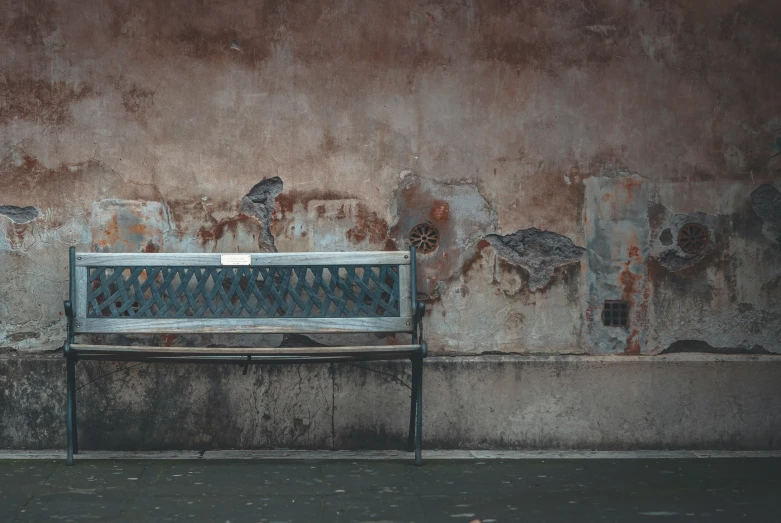 an old wooden bench in front of a rusted wall