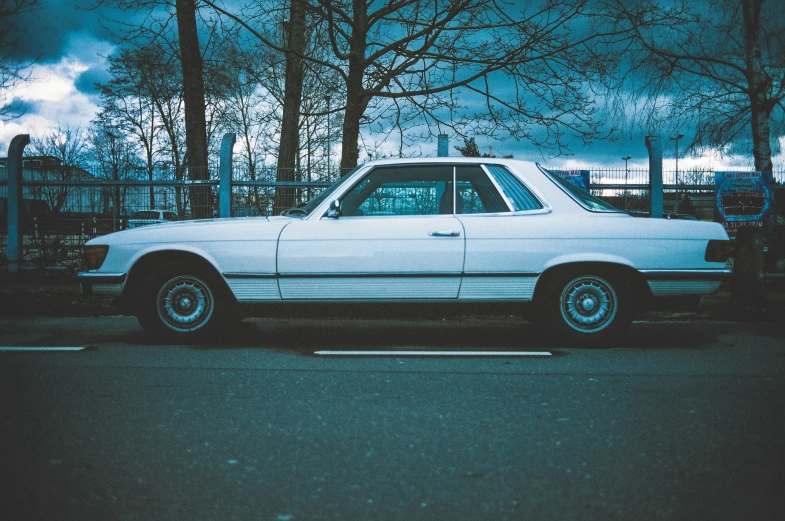 a white car sits parked next to some trees