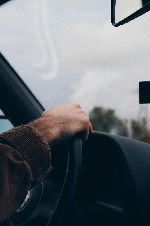 a man holding the steering wheel of a car in a cloudy sky