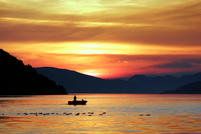 man rows boat across body of water during sunset