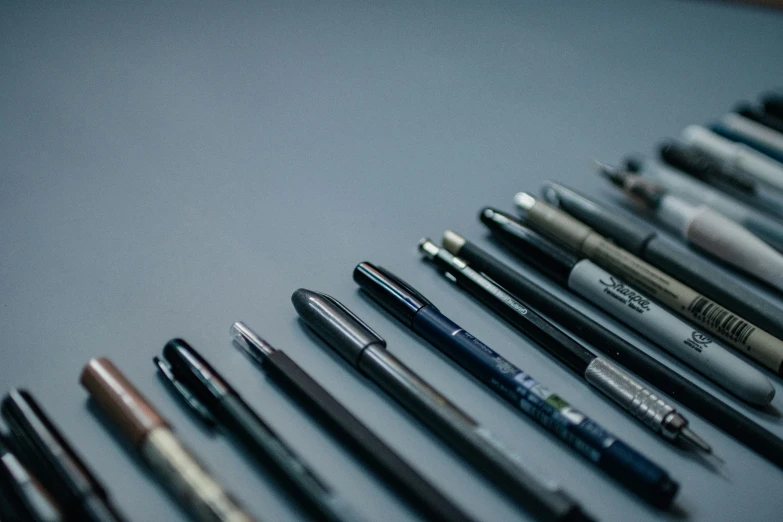 many pens lined up in a row on top of a counter