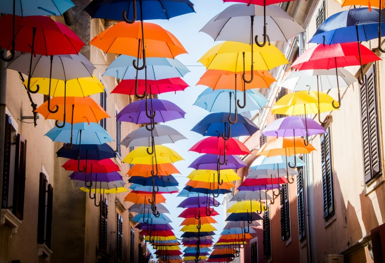 lots of multicolored umbrellas hanging over the streets of a city