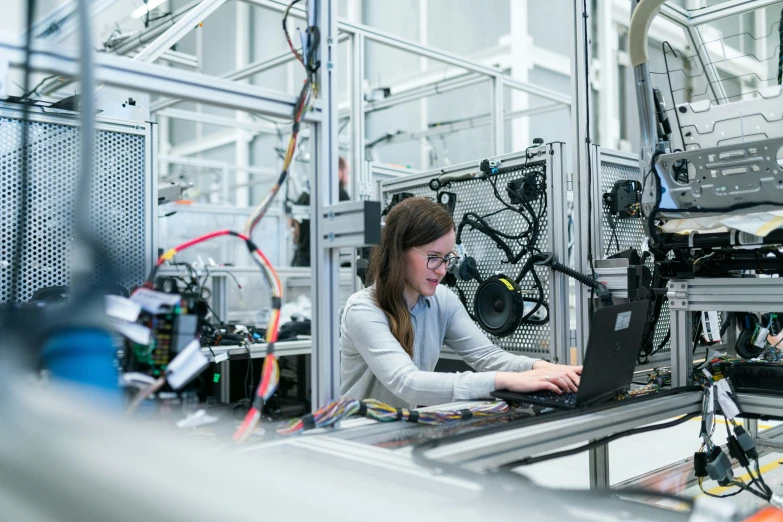 the woman is operating a laptop on the assembly line