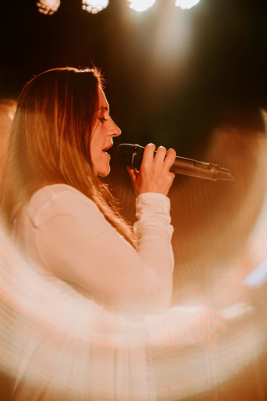 woman singing into microphone in darkened stage setting