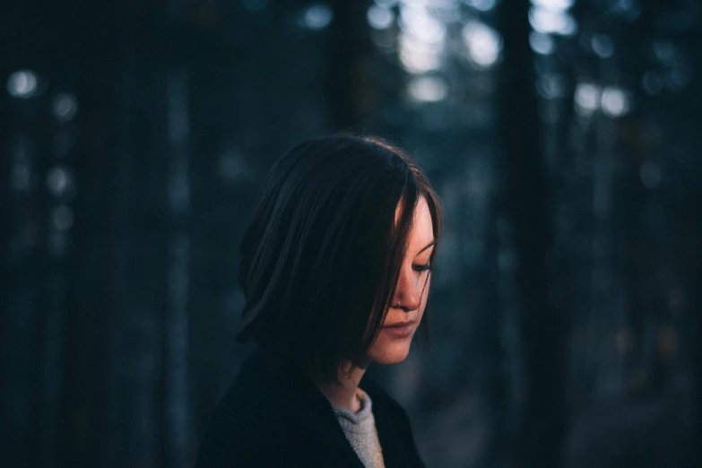 a woman in black coat with long dark hair standing in the woods